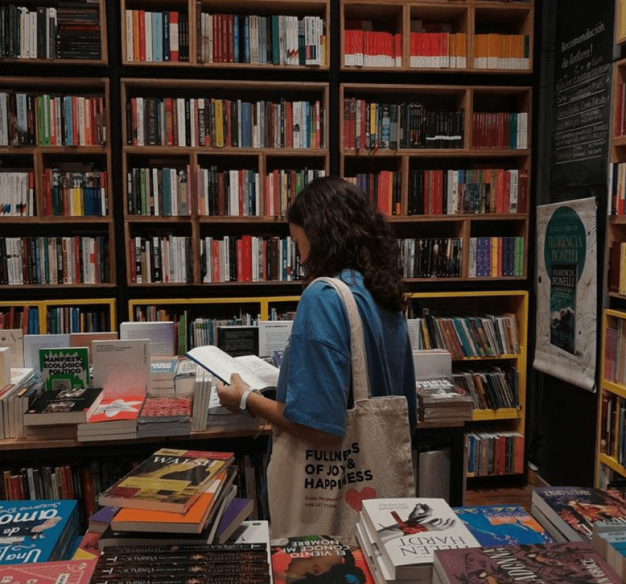 A reader leafing through a book in front of bookstore shelves