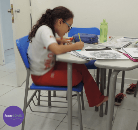 Criança sentada em sala de aula com os pés sem apoio no chão