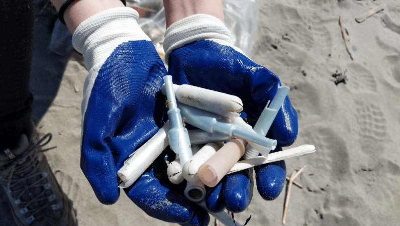 Mãos com luvas segurando aplicadores plásticos recolhidos na praia